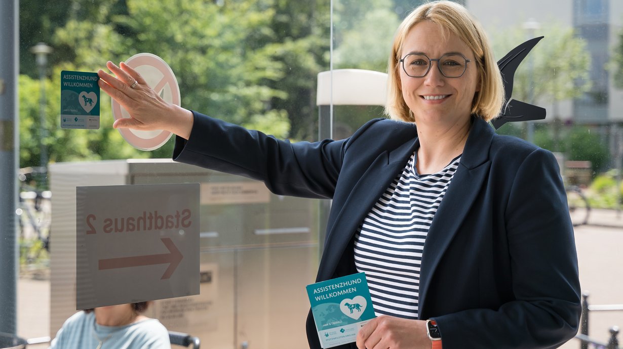 Osnabrücks Oberbürgermeisterin Katharina Pötter bringt den ersten „Assistenzhund willkommen”-Türaufkleber am Stadthaus 1 an.